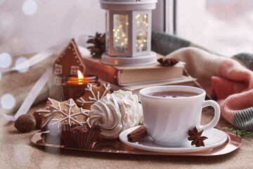 Cozy winter atmosphere at windowsill. Aesthetic Christmas window with books, gingerbread cookies, marshmallow, cup of espresso, candle cozy background