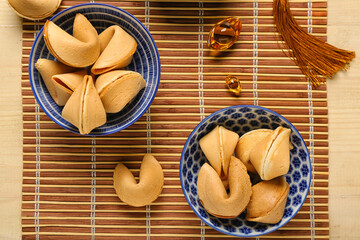 Bamboo mat with bowls of fortune cookies and Chinese symbols on wooden background