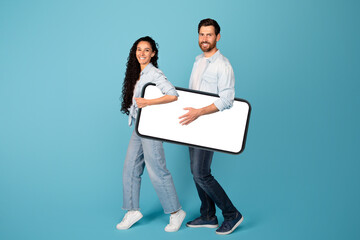 Smiling funny young european guy and woman in casual carry huge smartphone with empty screen