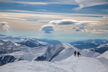 A couple of freeriders climb the mountains against a spectacular sky in Gudauri, Caucasus, Georgia