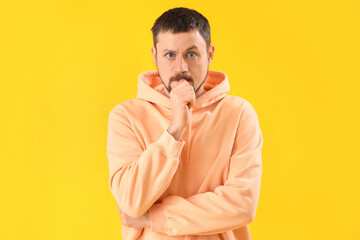 Handsome man in hoodie biting nails on yellow background