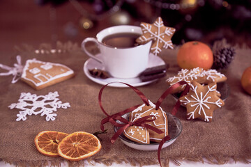 Obraz na płótnie Canvas Aesthetics Christmas ginger cookies, cup of coffee, tangerines near Christmas tree among decorations.