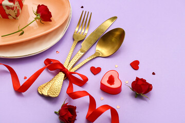 Table setting for Valentine's Day with golden cutlery, bow and hearts on lilac background
