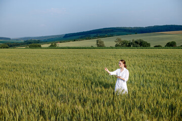Scientist technologist in a white coat on a young wheat field writes down data on this year's crop on a smart tablet