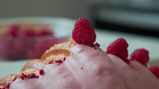 a hand decorates a raspberry croissant. a hand is laying raspberries on a croissant
