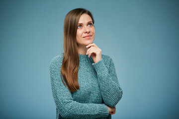 Smiling thinking woman in casual clothes touching her chin looking up. Advertising female studio portrait on blue.