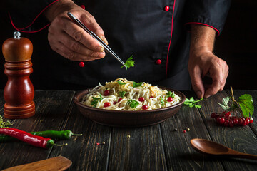 The cook puts parsley on a plate of spaghetti. Working environment in the restaurant kitchen. Delicious pasta with vegetables and spices. Copy space