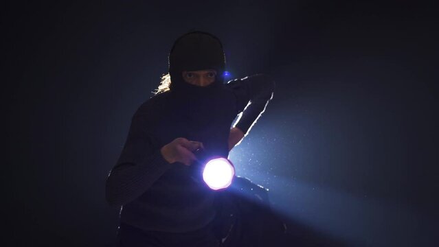 The robber holds the lantern around him. Thief.
The thief man with the bag is walking around with a flashlight in the dark room he entered for the robbery.
