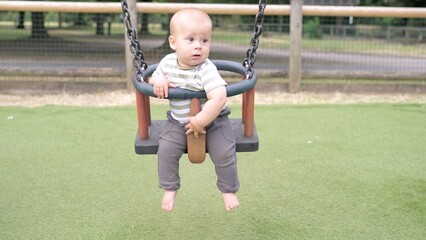 Fototapeta na wymiar Funny Little Younger Newborn Infant Brother Boy On Swing. Baby Playing On Playground. Summer time outside. Kids Entertainment, Childhood, Child Development, Happy Family Concept