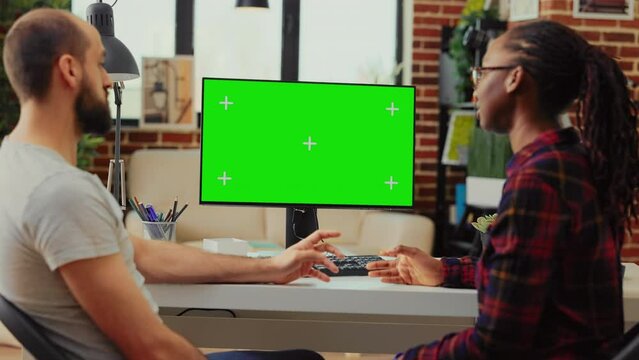Diverse team working on computer with greenscreen at desk, using monitor to examine isolated display and blank copyspace template. Analyzing mockup background on desktop screen.