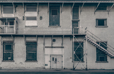 Facade of old two storey stucco penitentiary workshop building, paned windows with bars, fire escape, nobody