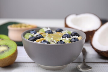 Bowl of delicious fruit smoothie served with fresh blueberries, kiwi slices and coconut flakes on white wooden table, closeup