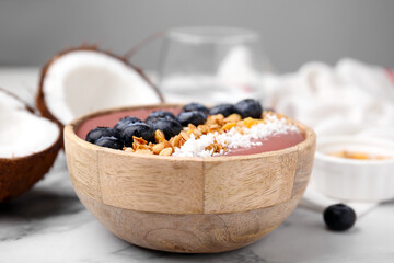 Bowl of delicious fruit smoothie with fresh blueberries, granola and coconut flakes on white marble table, closeup