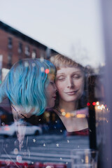lesbian couple photographed through window with city reflections