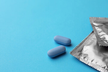 Pills and condoms on light blue background, space for text. Potency problem