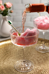 Pouring rose wine from bottle into glass with cotton candy on golden tray