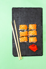 Fish sushi rolls with salmon, wasabi and chopsticks on black cutting serving board on green background with copy space. Seafood, Food service from restaurant concept