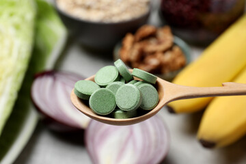 Wooden spoon of pills over table with foodstuff, closeup. Prebiotic supplements