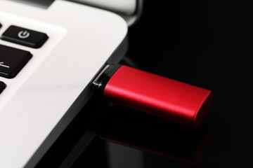 Modern usb flash drive attached into laptop on black table, closeup