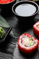 Tasty sushi rolls and soy sauce on black wooden table