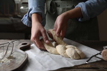 Woman making braided bread at wooden table indoors, closeup. Traditional Shabbat challah