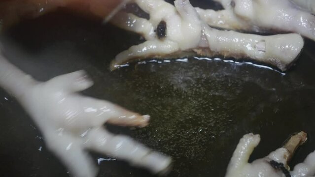 stirring chicken legs with cut claws in boiling oil in a frying pan, close-up