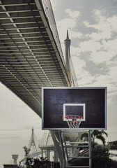 View of Basketball wooden backboard, Hoop orange metal ring and white netting against suspension bridge and sky background in the downtown park city. Empty basketball basket, Space for text, Selective