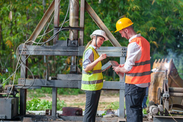 Male and female industrial engineers in Hard Hats discussing new projects while using laptops. They make gestures as they work in a heavy industrial factory.