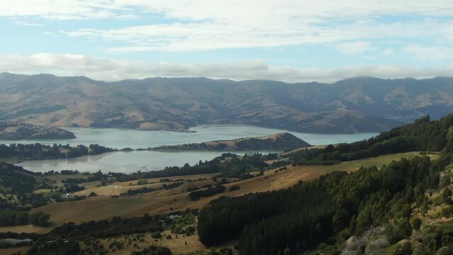 Aerial shot over the bay of Akaroa in New Zealand with lake surrounded by huge mountains and hills with varying terrain
