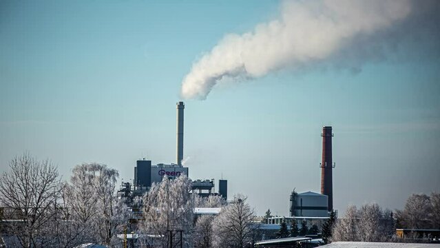 Timelapse shot of white smoke of a large factory surrounded snow covered landscape on a cold winter day.