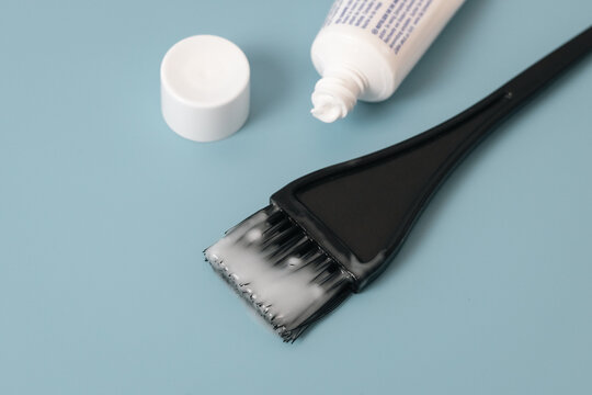 Brush for coloring hair and white paint with a tube on blue.