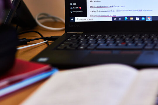 Windows laptop PC computer on wooden desk with notebook, files, folders and cables. Wordpress website builder on screen. Closeup with shallow depth of field, soft focus.