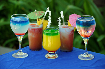 Five glasses of cocktail on a blue covered table and green background