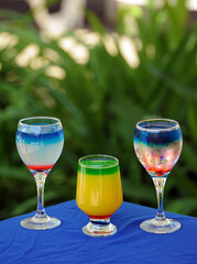 Three glasses of cocktail on blue covered table and green background (your text on top of the image)