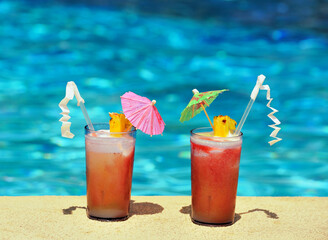 Obraz premium Two cocktail glasses by a poolside, blue water of a swimming pool, copy space 
