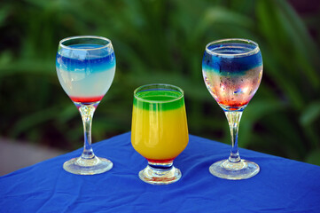 Three glasses of cocktail on blue covered table and green background with copy space