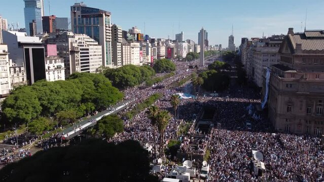 Thousand Fans celebrating Win of Soccer World Cup on 9 De Julio Avenue with Obelisco Obelisk Statue in background during sunny day with blue sky - Crowd Waving Argentinian Flag after triumph 
