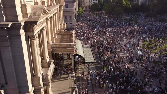 Aerial panning shot showing crowd of People cheering and escalate after Win of World Cup in Qatar - Climbing on facade of Col&oacute;n Theatre in Buenos Aires at sunset