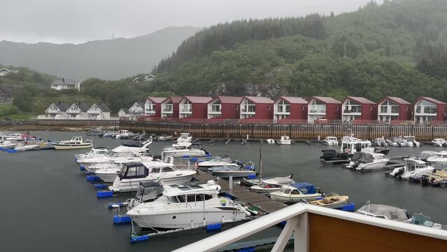 Medium static shot of a small town next to a marina on a rainy day with hills covered in green trees and bushes in the background