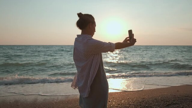 beautiful girl on the beach at sunset. a girl takes a selfie on the ocean at sunset. a girl takes a photo on the sea