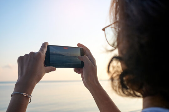 Woman taking pictures of beach, sea and resort at sunrise He used his phone to take high-angle shots. Travel concept and technology