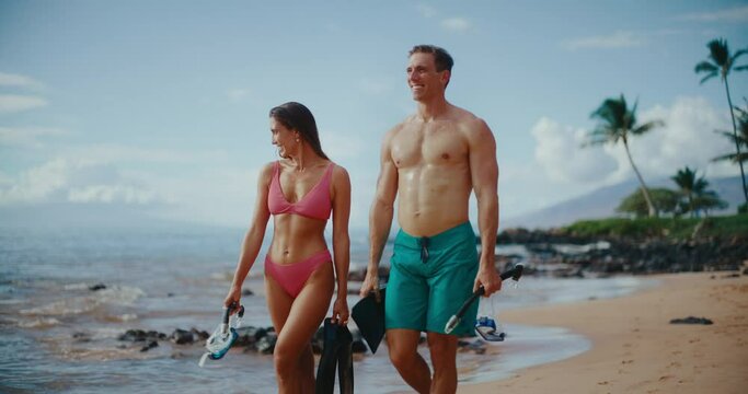Attractive couple walking down the beach with snorkel gear on tropical beach vacation