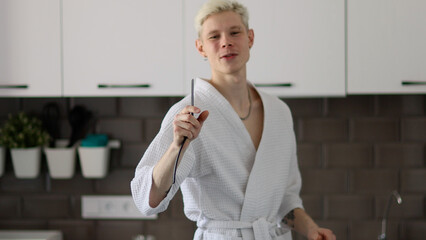 Young handsome happy man having fun in kitchen, listening to music and singing using kitchen spatula instead of microphone
