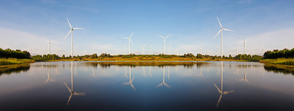 Powerful Wind turbine farm for pure energy production on Beautiful clear blue sky with white clouds and wind turbine farm reflection on lake. renewable energy	