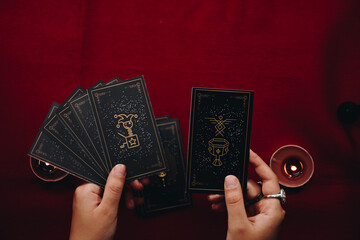 Fortune teller woman and black tarot cards over red table background and candles.