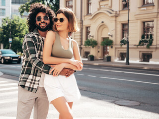 Fototapeta premium Smiling beautiful woman and her handsome boyfriend. Sexy cheerful family having tender moments in the street at sunset. Multiethnic models hugging. Embracing each other. Love concept. In sunglasses