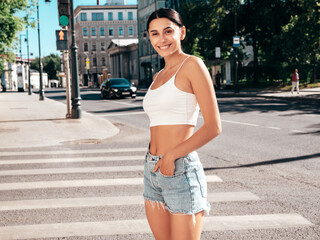 Young beautiful smiling hipster woman in trendy summer white top and shorts clothes. Sexy carefree model posing in the street at sunny day. Positive brunette female. Cheerful and happy