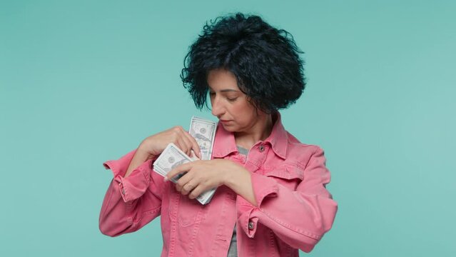 Mature serious woman with short dark curly hair trying to hide money in the pockets. Happy beautiful female 40s counting dollar bills and sniffs smell of fresh new banknotes. Slow motion people studio