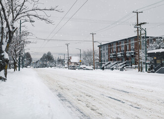 Naklejka premium Empty snow covered main street during snow storm. No traffic on snowed in city road. Deep slush and ice on road not serviced or plowed. Arctic winter blast. Vancouver, BC, Canada. Selective focus.