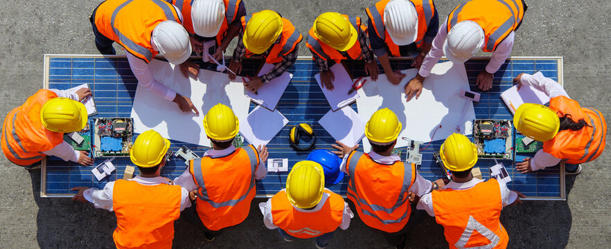 Team young man and woman architects and engineer working on solar panel and his blueprints with Solar photovoltaic equipment on factory construction site. meeting, discussing,designing, planing, 